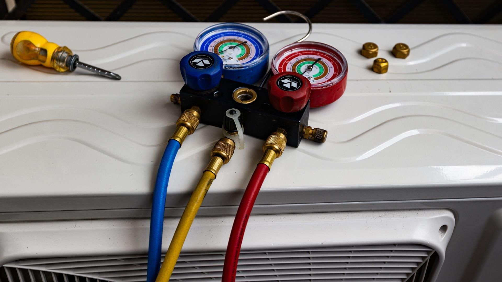 HVAC manifold gauge set with blue and red dials, brass fittings, and colored hoses on white surface.